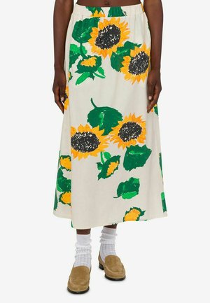 Gonna crema di media lunghezza con grandi stampe di girasoli gialli e foglie verdi, indossata con calzini bianchi e mocassini marroni.