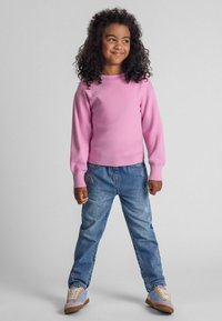 Rosa stickad tröja med långa ärmar och ribbad nederkant, tillsammans med ljusblå jeans med broderade regnbågar och stjärndetaljer.