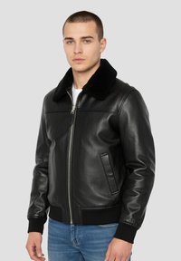 Giacca bomber in pelle nera con morbido colletto in pelliccia nera, cerniera frontale e polsini a coste. Presenta tasche laterali e una texture liscia.