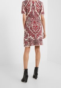 Rotes und cremefarbenes gemustertes Kleid mit kurzen Ärmeln, floralen Motiven und einer taillierten Silhouette, kombiniert mit schwarzen Knöchelstiefeln.