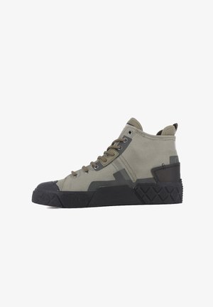 Zapatillas altas de lona verde tierra con puntera de goma negra y suela texturizada. Presenta ojales de metal y una lengüeta en la parte trasera.