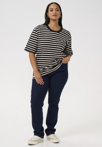 Sort og beige stribet t-shirt med rund halsudskæring, parret med mørkeblå jeans og hvide sneakers. Afslappet pasform og korte ærmer.