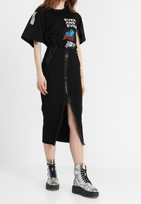 Svart grafisk T-shirt med korta ärmar, med färgglad text och mönster, tillsammans med en svart midi kjol med dragkedja fram. Silver plattform stövlar.