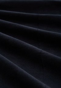 Tessuto in corduroy nero con una distintiva trama a costine, caratterizzato da pieghe morbide e una leggera lucentezza, presentato in una visione ravvicinata.
