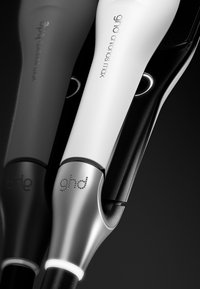 Gros plan sur un fer à coiffer ghd Chronos Max blanc et argenté avec un anneau lumineux et une surface réfléchissante sur fond sombre.