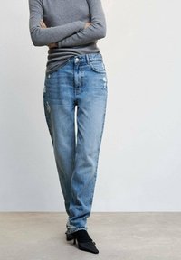 Jeans bleu clair délavés à la coupe décontractée, avec des déchirures au niveau des cuisses. Associés à un haut gris à manches longues et des talons noirs pointus.