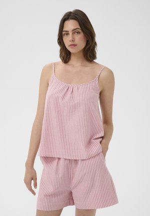 Jeune femme aux cheveux bruns mi-longs portant un top sans manches rayé verticalement rose et blanc avec un short assorti.