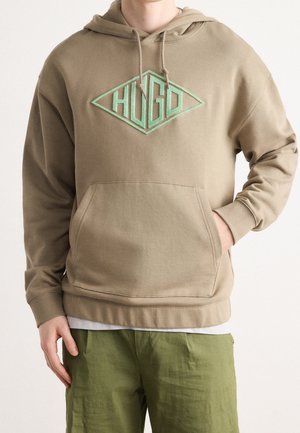 Kaki hoodie med huva och en framficka. Har en teal färgad diamantformad logotyp "HUGO" i mitten. Sytt i detaljer är synliga.