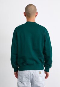 Grøn crewneck sweatshirt lavet af glat stof, med ribbede manchetter og kant. Båret med lysegrå cargo-bukser.