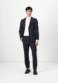Traje de marinero con un diseño ajustado, hecho de una tela suave, combinado con una camisa blanca. Zapatos negros pulidos completan el look.