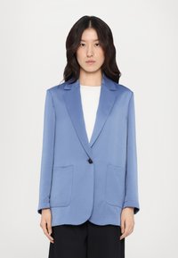 Lyseblå blazer laget av mykt stoff, med en enkelt svart knapp, to frontlommer og en strukturert kragedesign.
