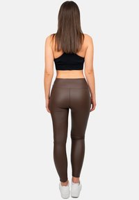 Leggings in ecopelle marrone con vita alta, texture liscia e design aderente, abbinati a un top corto nero e sneakers bianche.