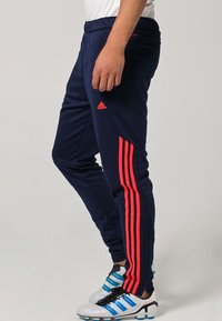 Tmavě modré sportovní kalhoty s červenými pruhy po stranách, elastickým pasem a zúženým střihem. Vyrobené z hladké, lehké látky.