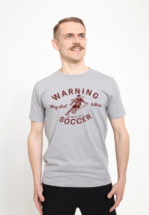 Camiseta de algodón gris con una impresión roja que dice "ADVERTENCIA Puede empezar a hablar de FÚTBOL" y una ilustración de un futbolista.