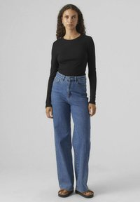 Schwarzes Langarmshirt, kombiniert mit hochtaillierten, weit geschnittenen blauen Jeans. Glatte Baumwolltextur; Denim mit leichtem Verblassen und sichtbaren Nähten.