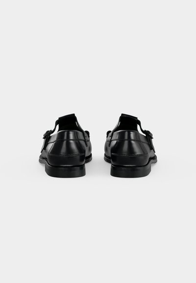 Paire de chaussures habillées en cuir noir avec boucles, vues de dos sur un fond blanc uni.