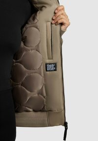 Rudas pūkinis džemperis su siuvinėta vidine dalimi, užtrauktuku, šonine kišene ir etikete. Lygus paviršius ir banguotas apačios detalių dizainas.