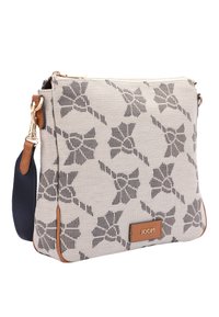 Beżowa torba na ramię z płótna z czarnym wzorem kwiatowym, brązowymi skórzanymi akcentami, złotymi elementami i regulowanym granatowym paskiem.