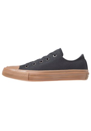 Lavtop sort lærreds-sneaker med seks metaløjer og brun gummisål og tåhæt, vist i sideprofil.