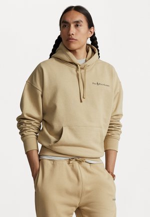 Bež kapuutsviiter, mis on valmistatud pehmest kangast, esiosas suurtasku ja nöörid. Rinnal tikitud logo.