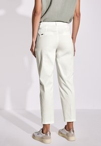Pantaloni bianchi in cotone con taglio dritto, dotati di una parte frontale piatta, tasche posteriori e passanti per cintura. Abbinati a sneaker beige.