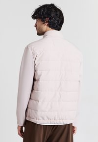 Helle rosa Daunenjacke mit glatter Textur, hohem Kragen, segmentiertem Steppmuster auf dem Rücken und slim fit.