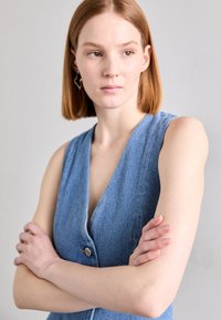 Denim ilmanhiha-asu, jossa on syvä V-muotoinen kaula-aukko ja yksittäinen nappikiinnitys. Vaaleansininen väri, sileä pinta ja tiukka malli.