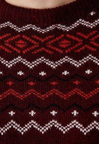Suéter de punto con una base color burdeos que presenta patrones geométricos en rojo y blanco. Diseño texturizado con un cuello y puños de canalé.