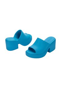 Mules en caoutchouc bleu avec un bout ouvert, une large lanière supérieure et un épais talon bloc. Texture lisse et design minimaliste.