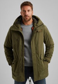 Maslinasto zelena parka jakna s kapuljačom, prednje zatvaranje na zip, dva velika džepa i rebrasti manžeti. Ima mekani unutarnji oblog.