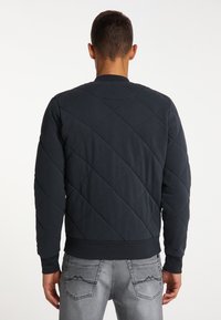 Mörkblå kviltad sweatshirts med diamantsymmetri, ribbade mudd och nederkant. Baksidan har en enkel och strömlinjeformad design.