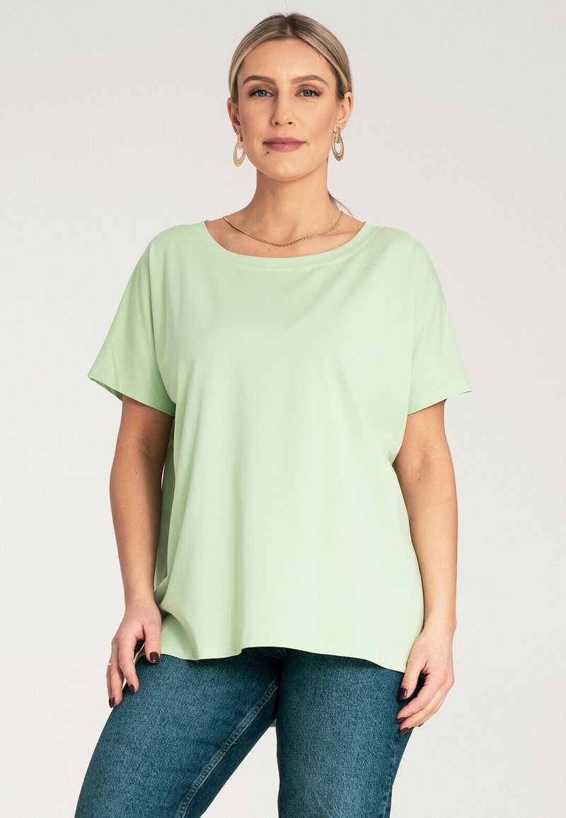 Jasnozielona bluzka z krótkim rękawem z miękkiego materiału o luźnym kroju i okrągłym dekolcie, zestawiona z ciemnoniebieskimi dżinsami.