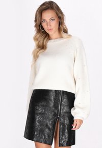 Pulover alb din tricot cu accente asemănătoare unor perle și mâneci lungi, asortat cu o fustă mini din piele sintetică neagră, prezentând un fermoar frontal și un finisaj texturat.