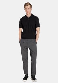 Czarna koszulka polo z krótkim rękawem, szare spodnie slim fit z plisami z przodu oraz czarne sneakersy z białymi podeszwami. Minimalistyczny design o gładkiej strukturze.