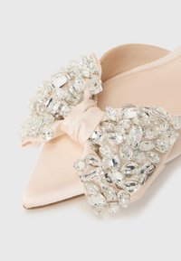 Pointed nude satin flat shoe with large decorative bow adorned with clustered clear rhinestones and beads on the toe area.