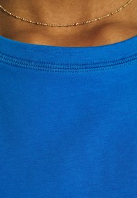 Camisa de algodón azul con un escote redondo, que presenta una textura suave y un dobladillo cosido limpio, resaltando su color vibrante.