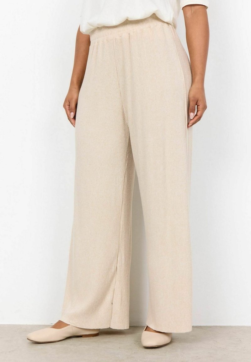 Beige ribbed wide-leg pants with an elastic waistband and side slit details, paired with light-colored flat shoes on a smooth surface.