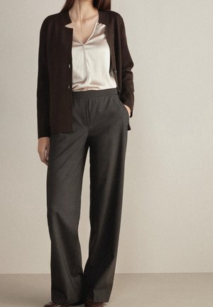 Pantaloni lunghi neri abbinati a un cardigan a maniche lunghe di un marrone scuro con apertura frontale e a una blusa in satin chiaro. L'outfit presenta una vestibilità rilassata e delle texture morbide.