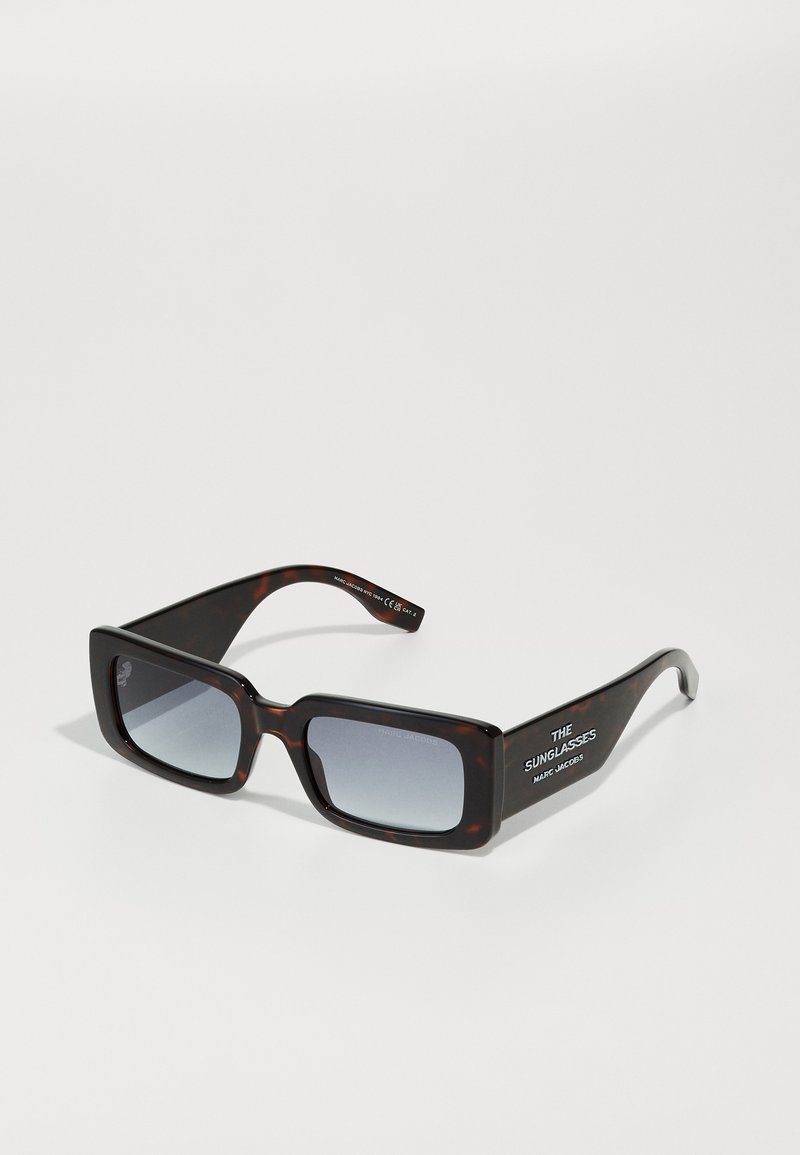 Gafas de sol de carey de gran tamaño con lentes grises degradados. Presenta un diseño de marco rectangular y texto de marca en blanco en las patillas.
