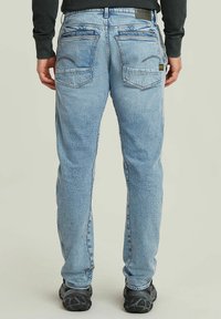 Jasnoniebieskie dżinsy o luźnym kroju, z dwiema tylnymi kieszeniami i delikatnym przetarciem. Wykończone czarnym obuwiem.