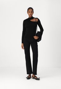 Un haut noir ajusté à manches longues avec un détail découpé et des manches évasées, associé à un jean noir taille haute et des chaussures plates noires.