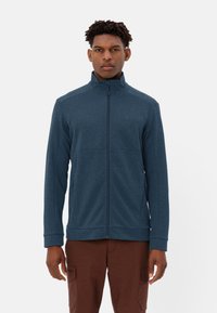 Giacca zip-up navy in tessuto testurizzato, colletto alto e due tasche frontali. Presenta polsini e orlo elasticizzati per un look aderente.