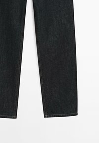 Gambe di jeans in denim blu scuro con taglio dritto e cuciture marroni visibili su uno sfondo bianco.
