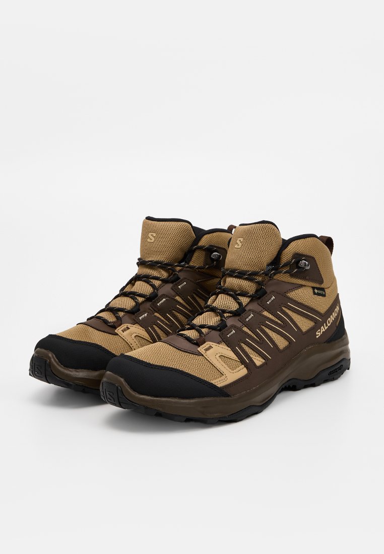 Botas de senderismo de caña alta en marrón y beige, que cuentan con materiales de malla y goma, una superficie texturizada y áreas reforzadas en la puntera y el talón.