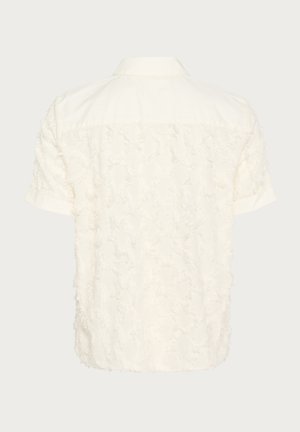 Kratka majica s kratkimi rokavi v off-white barvi, z teksturiranjem in raztrganim vzorcem na hrbtni strani, klasičnim ovratnikom in z gumbom za zapiranje.