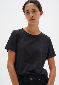 Tricou negru din bumbac cu guler rotund și mâneci scurte. Textură fină, croială lejeră, purtat cu pantaloni închisi la culoare, detalii minime.