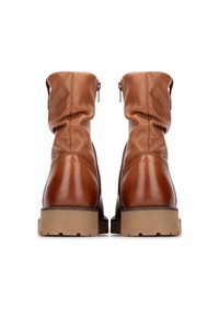 Botas de cuero marrón hasta el tobillo con un diseño caído, cremallera trasera y suelas de goma beige resistentes. Textura suave con discretos detalles de costura.