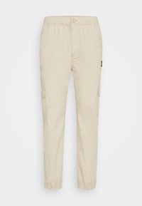 Pantalones cargo beiges hechos de tejido ligero, con una cinturilla elástica, bolsillos laterales tipo cargo y tobillos ajustados.