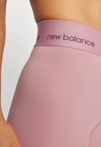 Close-up de uma pessoa a usar leggings mauves de cintura alta com uma cinta larga marcada com "new balance."