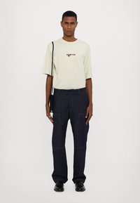 Hellgrünes kurzärmeliges T-Shirt mit roten Buchstaben, kombiniert mit dunkelblauen weit geschnittenen Jeans mit sichtbaren Nähten. Tragen mit schwarzen Schuhen und einer Tasche.